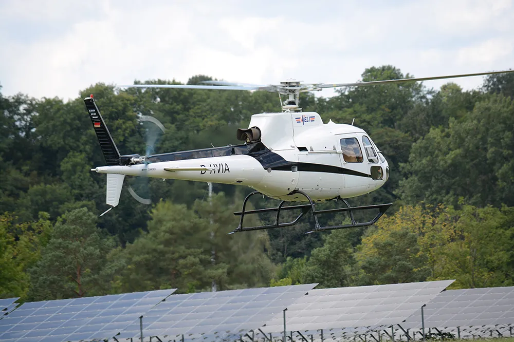 Weißer Hubschrauber im Tiefflug über einem Gelände