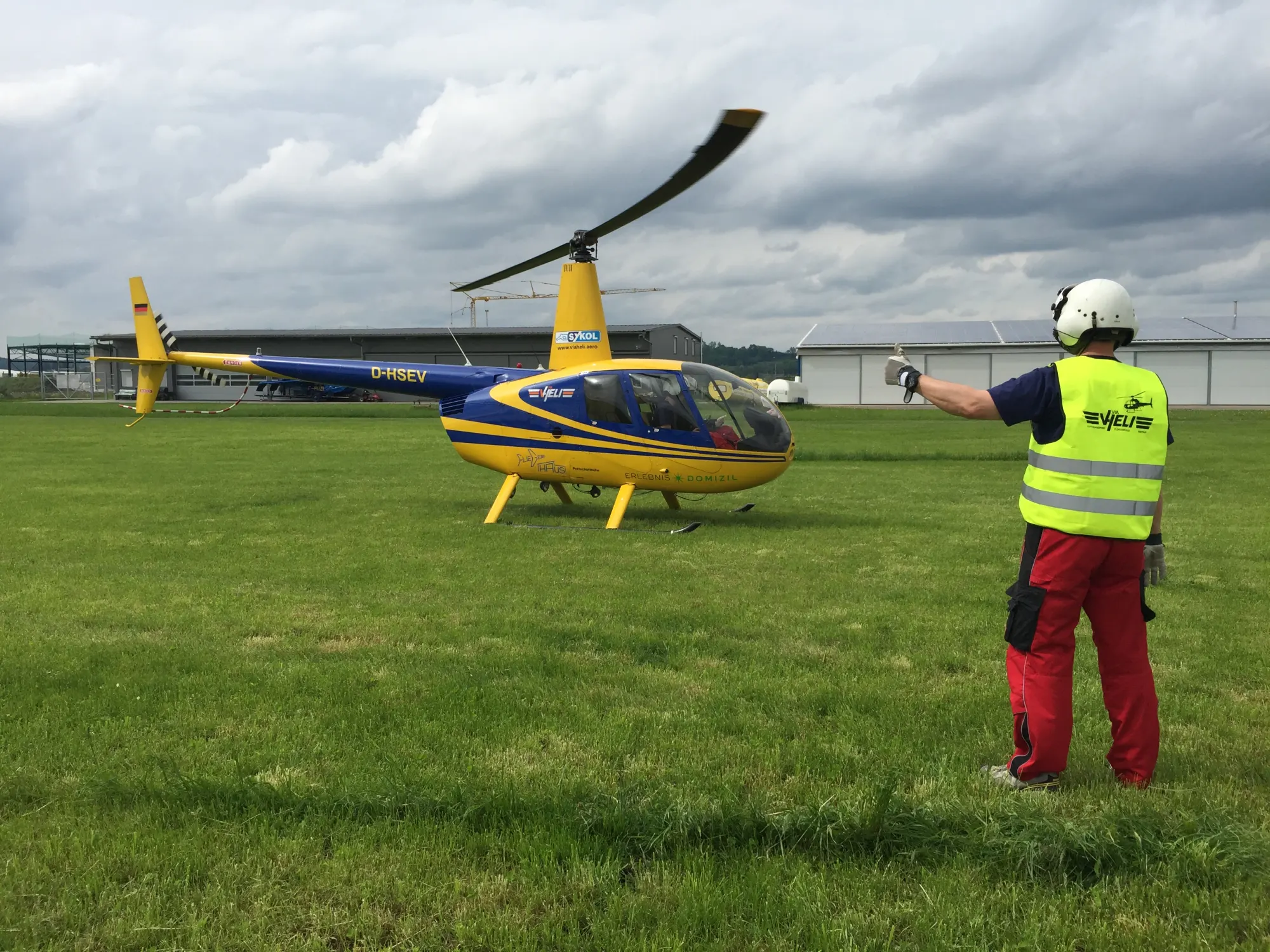 Gelber Hubschrauber auf einer Wiese, ein Einweiser in Warnweste steht davor