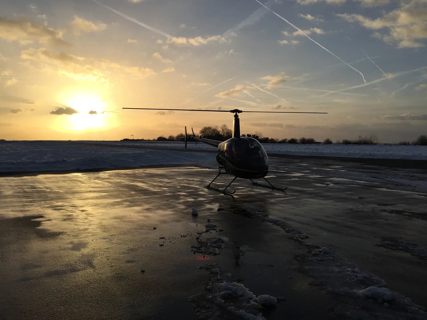 Hubschrauber auf nassem Vorfeld im Gegenlicht der tiefstehenden Sonne